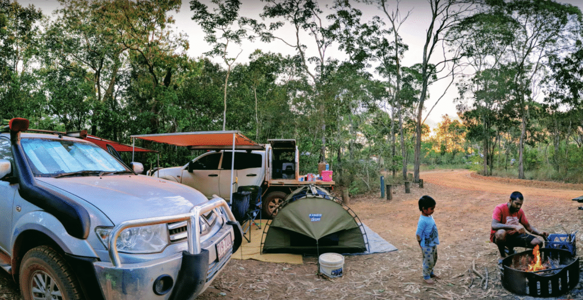Young enough to share a swag with mum and dad. A remote campsite at sunset with a silver 4WD, a small green dome swag, and a man tending a campfire while a child watches. Packing a tent is a great way to experience places like Eliot Falls if you're touring with an on-road van. 