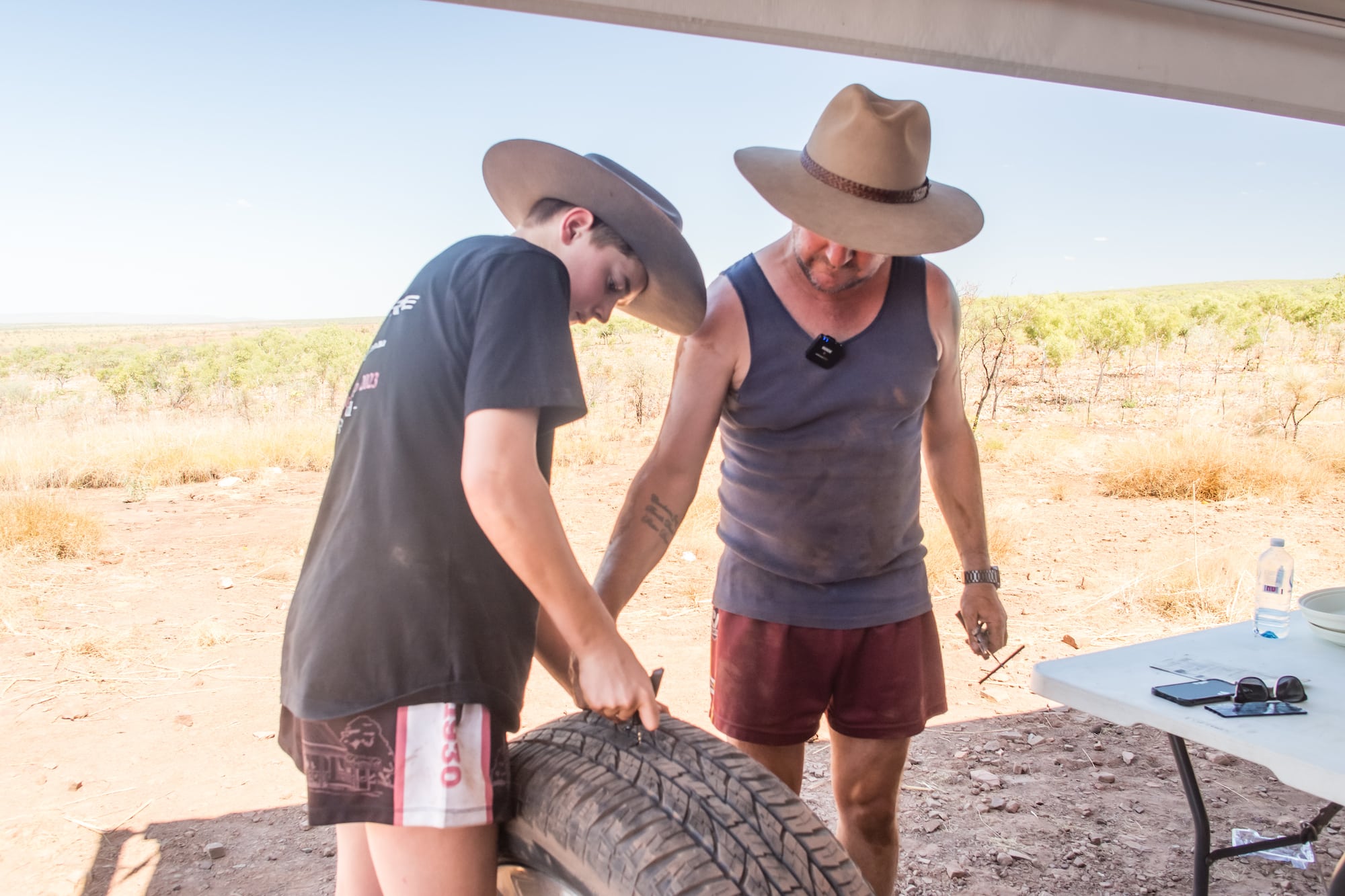 A father watches over his teenage boy plugging a tyre under an awning: location, the Gibb River Road