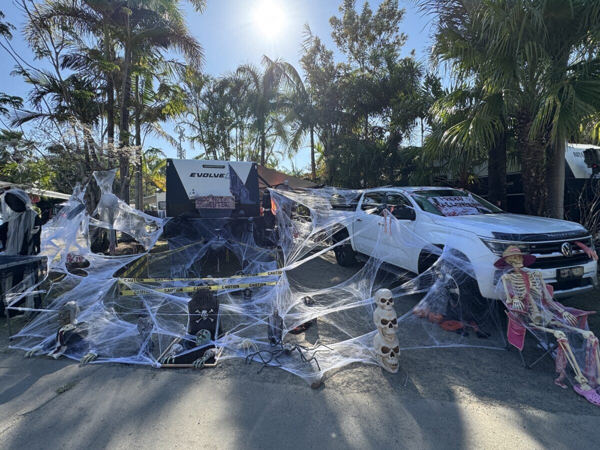 A caravan and tow vehicle parked up on a campsite at BIG4 Whitsunday Resort. Palm trees are in the background with the sund behind. Everything is covered in a fabric 'cobwebs' to celebrate Halloween at the parks Camp and sCare fundraising event
