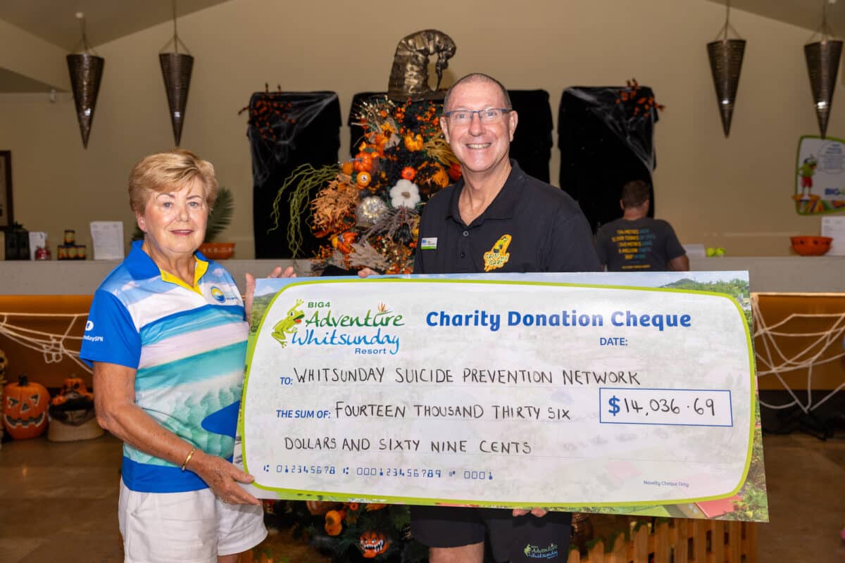 Two people hold a giant check indoors. The man standing behind the check is from the BIG4 Adventure Whitsunday Resort hands it to a woman on behalf of the Whitsunday Suicide Prevention 