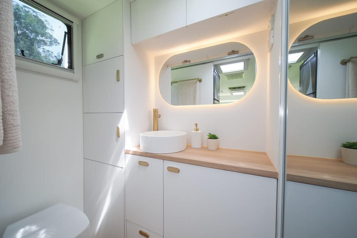 Ensuite interior. Here we see an oblong mirror above a circular fluted sink, white cabinets and a mirror door