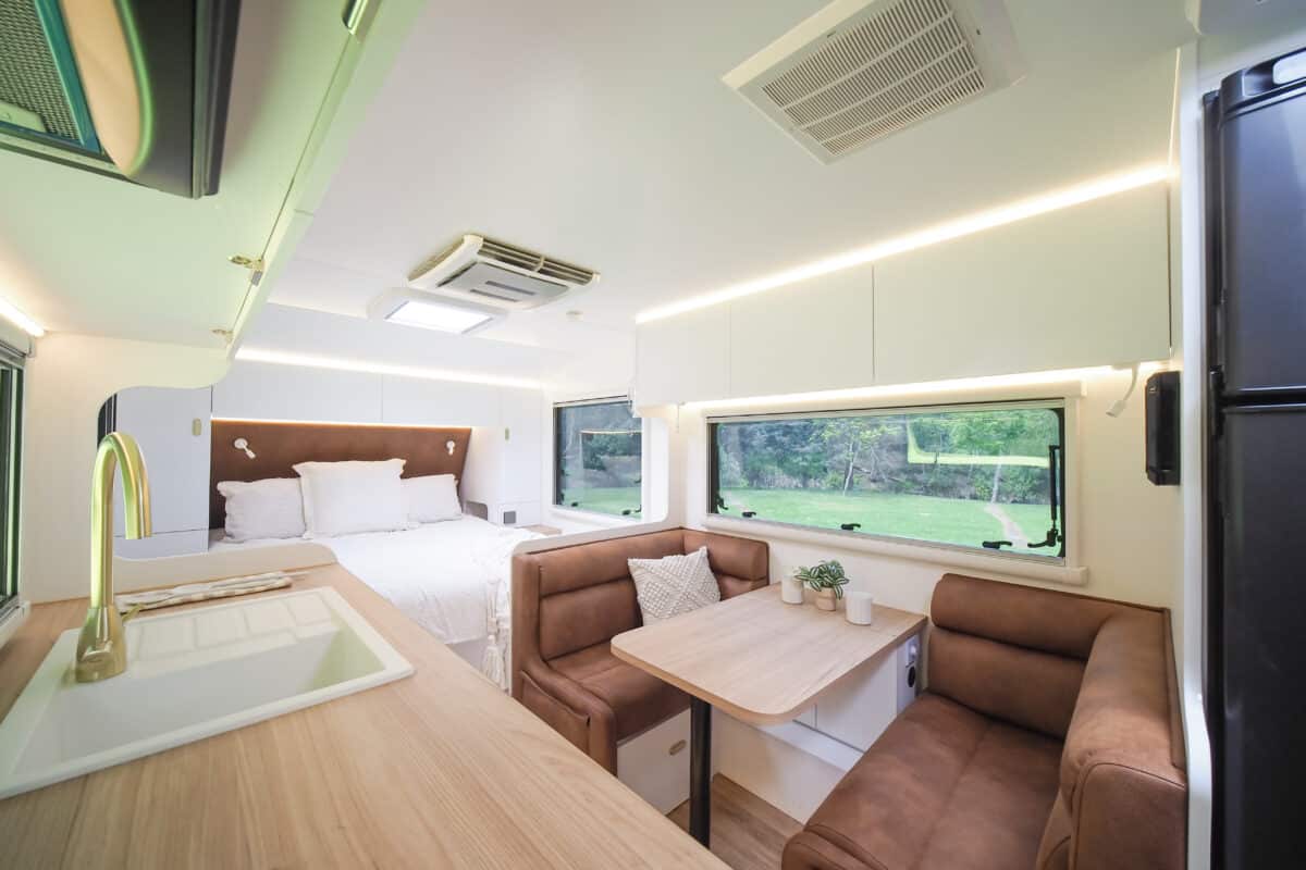 The Grand Caravans 2025 Peak 19 6 interior with a timber look benchtop on the left and lumber supported dinette lounge on the right