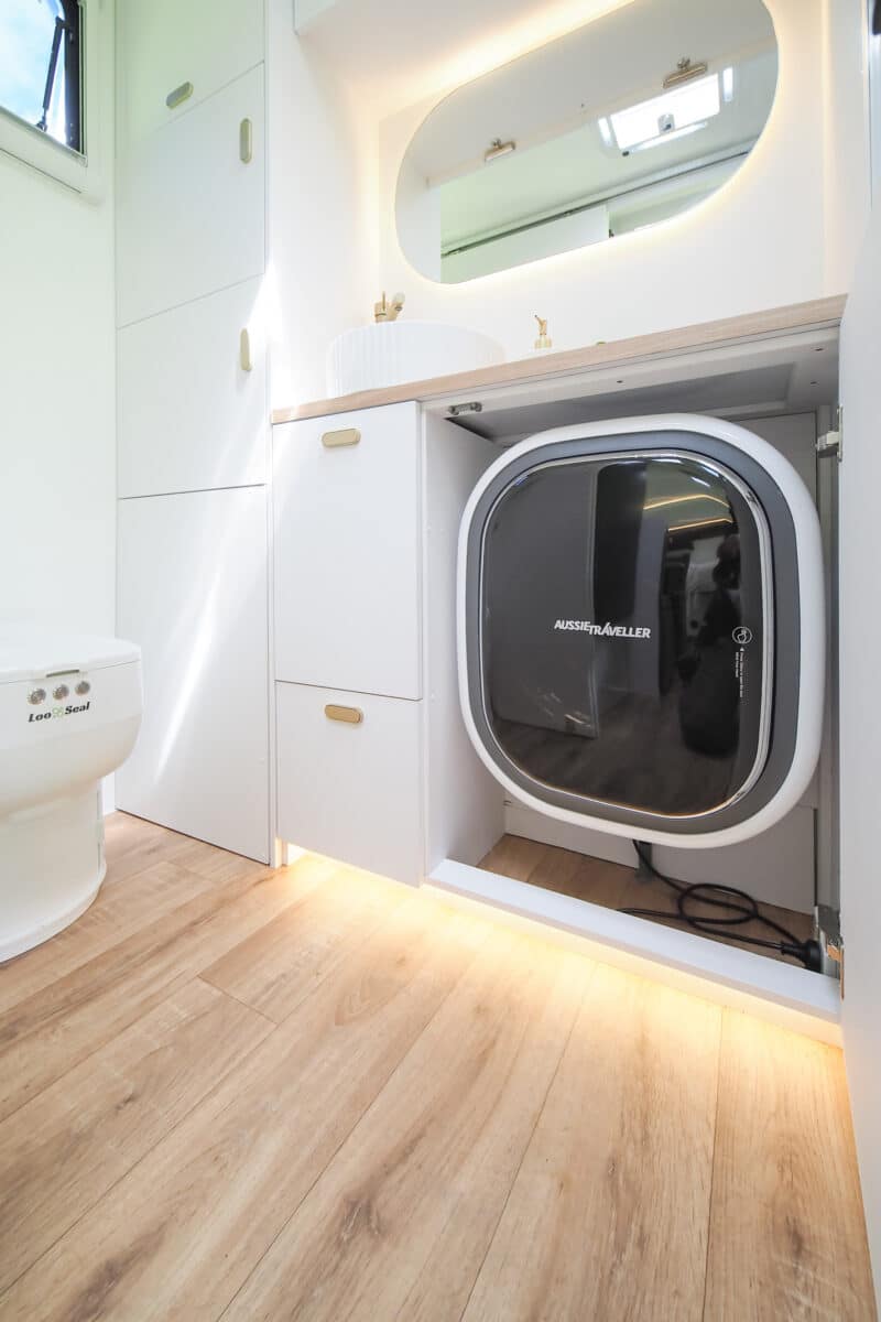 A floor shot of the ensuite with an open cabinet revealing a front loading washing machine