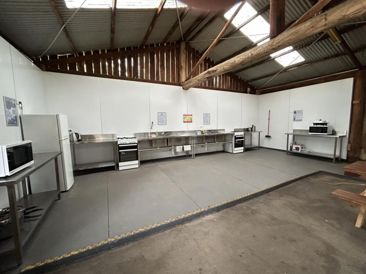 The newly renovated rustic camp kitchen at Lakes Bushland Caravan Park, featuring exposed beams, stainless steel benches, and new appliances.
