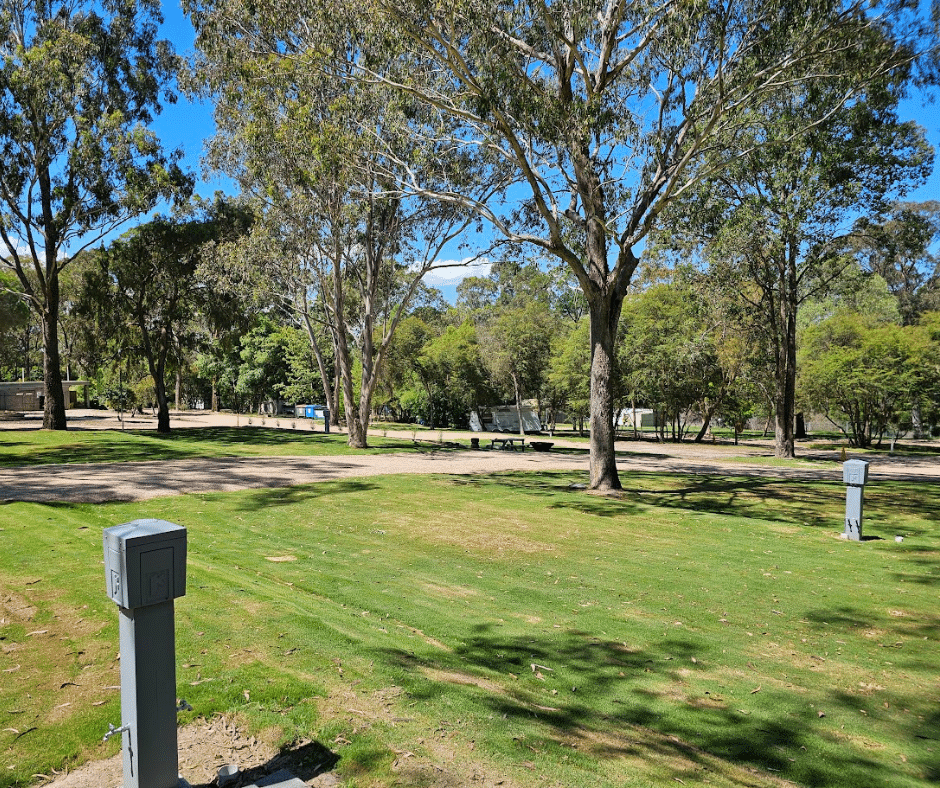 A view across the expansive, grassy powered sites with shade trees at Lakes Bushland Caravan & Lifestyle Park.