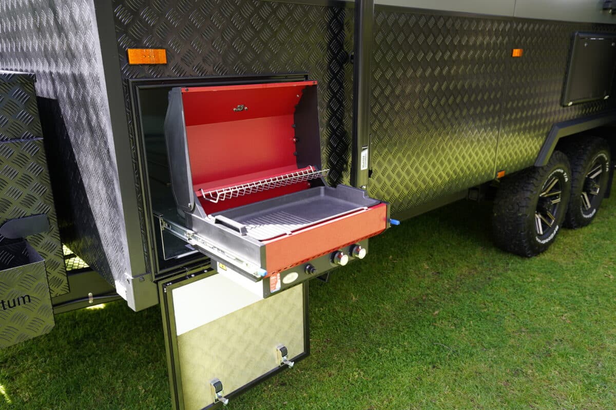 A close up of a red pull-out barbecue on the outside of the Momentum Velocity caravan