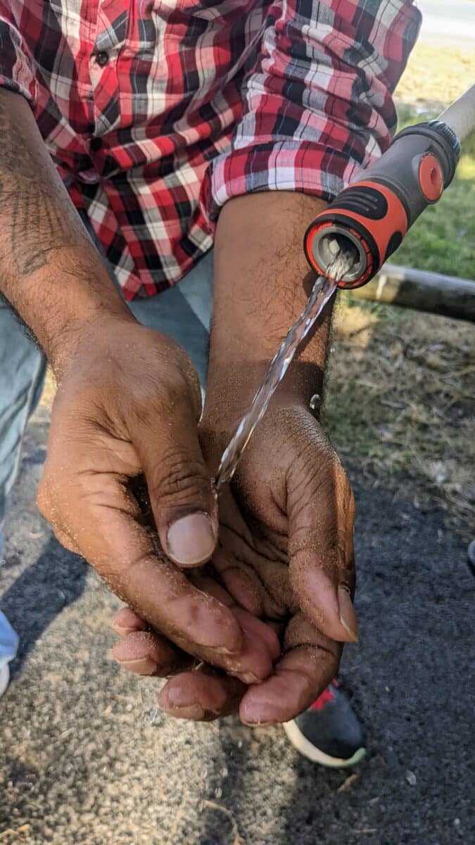 Washing sandy hands with a DIY jerry can hose control valve setup.