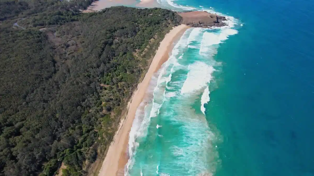 Aerial view of a sandy beach and rugged coastline along the Sapphire Coast in summer