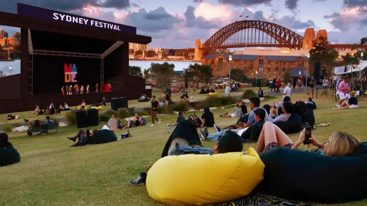 People relaxing on the grass at an outdoor Sydney Festival event with the Sydney Harbour Bridge behind them