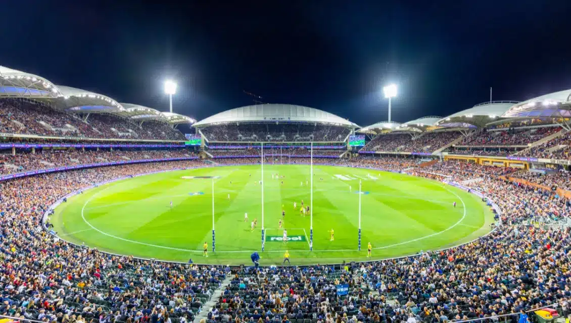 large afl stadium filled with people wide view lights on at night