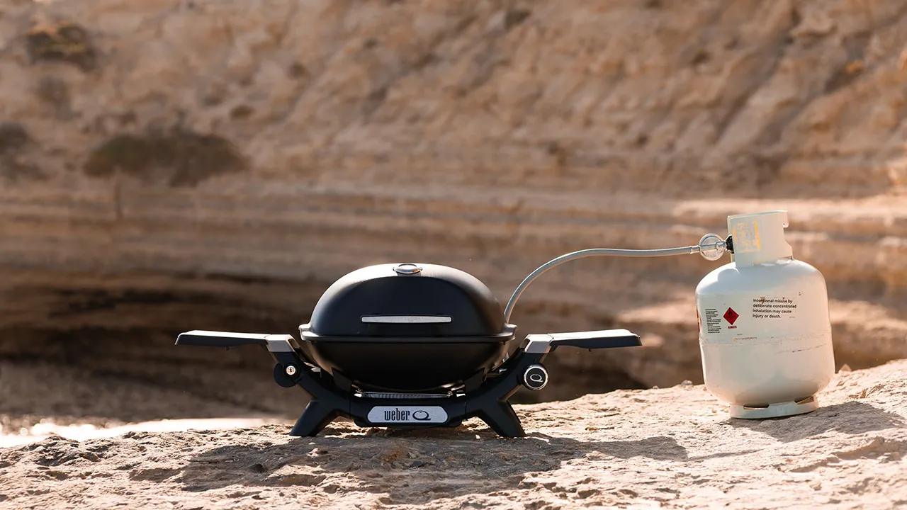 portable bbq sitting in outdoor scene connected to gas bottle