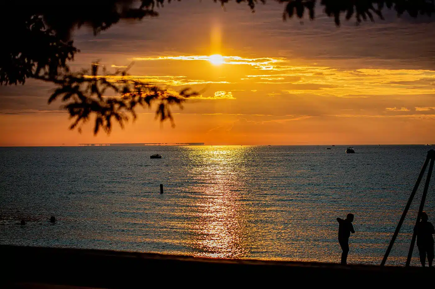 Mindil Beach in Darwin at sunset during the dry season, with orange and pink sky reflected on the water and silhouettes of visitors on the sand.