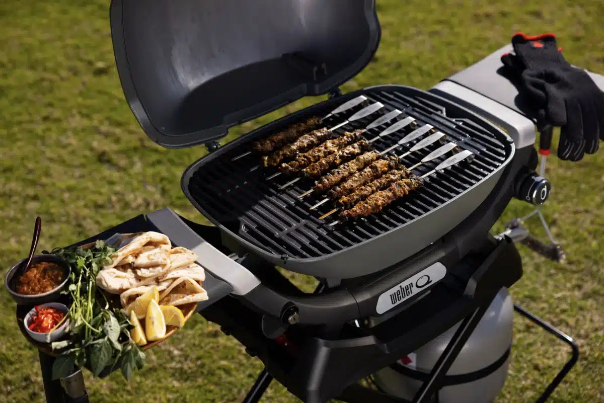 Weber Q portable BBQ grilling meat skewers outdoors with flatbread, lemon and fresh herbs on the side table